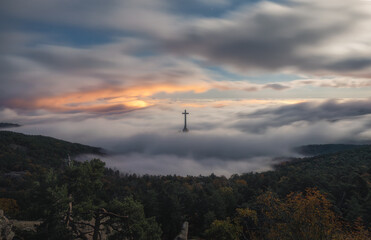 Obraz premium Cross rising above foggy forested landscape near Madrid