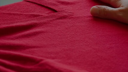 Close-up of human hand gently touching red wool jumper. Texture, softness, comfort and tactile sensation of natural woolen garments
