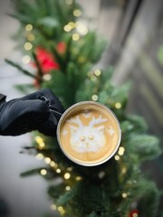 A warm latte art surrounded by pinecones, red and gold holiday decor, and blurred Christmas tree lights in the background. Perfect for holiday promotions, seasonal marketing and festive discounts.