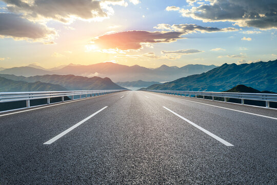 Empty asphalt highway road leading towards the distant mountain range at sunset