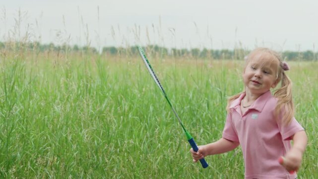 white girl exploring grass in meadow, bending to examine plants and shuttlecock, gentle calm atmosphere with tall green stems, pink polo and denim shorts, thoughtful summer wonder in countryside