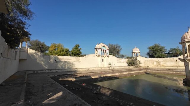 A scenic wide-angle view of a traditional heritage pond in Rajasthan near Mandawa, featuring beautiful stone chhatris and ornate pavilions under a clear sky