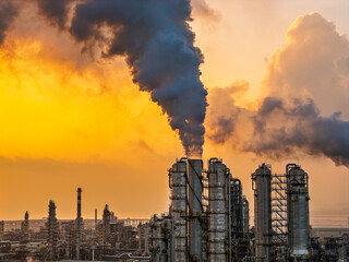 Large industrial oil refinery and chemical plant with smoking chimneys at golden sunset