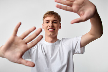 Fototapeta premium Hands, smile, young, man, framing, forward, whiteshirt, playful composition open gesture friendly mood in studio setting with bright light for casual lifestyle and youth engagement