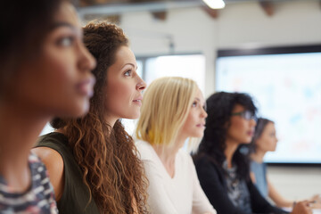 Close up of a Group of women attend marketing presentation. Audience watches projection screen with sustainability presentation . Professionals learn in classroom setting. Teamwork, education, strateg