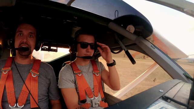 Pilot preparing for flight in a small aircraft cockpit, adjusting equipment and securing harness, showcasing the excitement and anticipation before takeoff in a vibrant sunset atmosphere