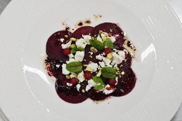Fototapeta premium sliced beetroot appetizer with goat cheese and fresh herbs, close-up view, served on a white plate, modern restaurant cuisine,