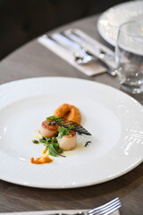 Close-up view of a gourmet appetizer with seared scallops served on a white plate in a fine dining restaurant. Elegant presentation with herbs, sauce, and pur&eacute;e highlights modern European cuisine and 