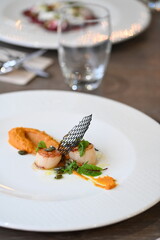 Close-up view of a gourmet appetizer with seared scallops served on a white plate in a fine dining restaurant. Elegant presentation with herbs, sauce, and pur&eacute;e highlights modern European cuisine and 