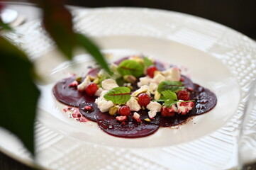 sliced beetroot appetizer on a white plate, goat cheese and fresh herbs, healthy vegetarian food, close-up view, elegant food presentation,