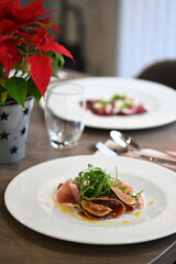 close-up view of served food, sliced Parma ham, fresh arugula and figs with dressing, light plate on restaurant table, elegant gourmet appetizer,
