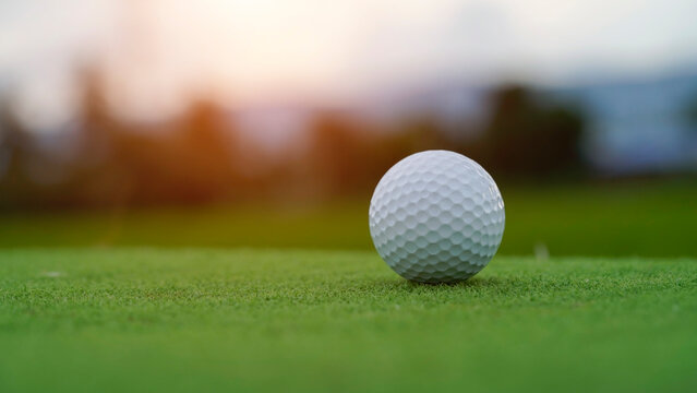 Golf ball on green grass in the evening golf course with sunshine background.