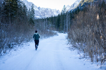 Person running alone on a snow-covered path surrounded by winter forest and mountains