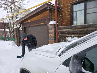 Man brushing snow off white car in winter weather, concept of vehicle maintenance and cold season challenges, cleaning, automobile care.
