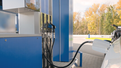 White car refuels at modern gas station with blue pump. Fueling vehicle energy demand and transportation concept.