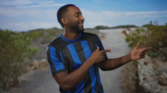 Man wearing blue and black striped soccer jersey with finger pointing to object in forest; playful supporter pride.