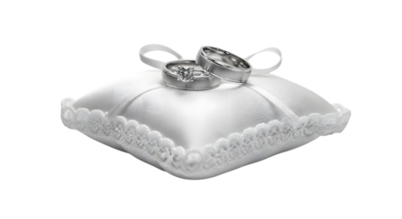 Two silver wedding rings with diamonds resting on a white satin ring pillow with lace trim isolated on a transparent background