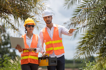 Engineer wearing safety vests and helmets analyzing wind energy data on laptop at wind farm, representing teamwork and sustainable technology development.