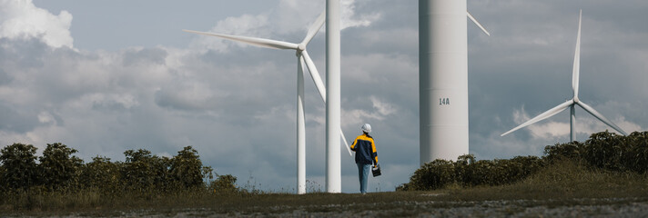 Female wind turbine technician standing with laptop and toolbox at wind farm, representing renewable energy maintenance, green technology, professional engineering in clean power.