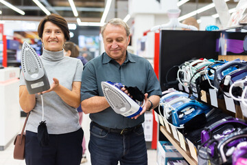 Mature couple choosing new clothes iron in electronic department hypermarket