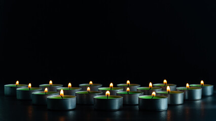Multiple burning tealight candles arranged in a row against a dark background, symbolizing remembrance, peace, spirituality, unity, and calm atmosphere with copy space.