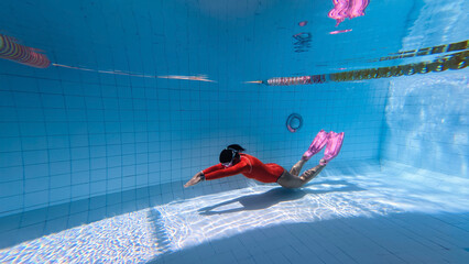 Young woman with mermaid tail swims and dives under sunlit deep water