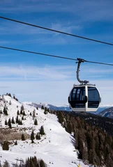 Fototapete Rund Gondeln Modern cable car gondola over a snowy alpine ski resort with pine forest and mountains under clear blue sky. Winter travel, ski holiday and mountain transportation concept in the Alps.  © Nadia