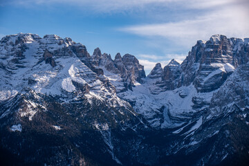 Dramatic winter view of snow-covered alpine mountain peaks with rugged rock formations under a clear blue sky. Scenic alpine landscape, winter season, wilderness and natural beauty in the Alps.