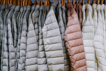 Multi-colored warm down coats or down jackets hang on wooden hangers in clothing store.