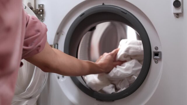 Female individual loading a washing machine with white towels, demonstrating the process of laundry preparation, showcasing the action of placing items inside the drum