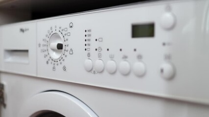 Hand adjusting washing machine settings, turning dial and pressing buttons, initiating laundry cycle, with clear display of time and program indicators on control panel