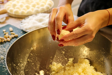 Hands shaping homemade coconut truffle over metal mixing bowl