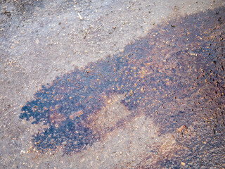 Oil stain on asphalt road surface with wet texture and gravel. Close-up detail of pollution on pavement, photographed outdoors, showing surface damage and contamination.