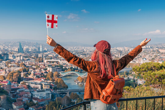 Cheerful woman holding a Georgia flag enjoying the panoramic view of Tbilisi cityscape and the Kura River
