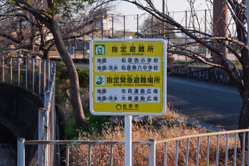 大阪府松原市の防災看板：地震と洪水で異なる避難先（西小・六中・運動広場）を記した区分表示 © 大出正一