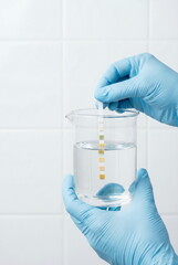 Scientist in blue gloves tests water quality with a pH strip in a lab beaker, symbolizing purity and research.