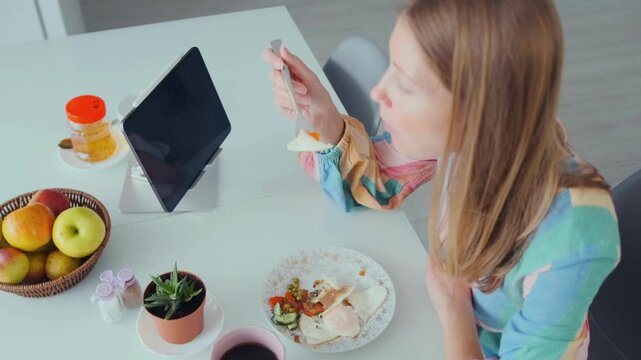 woman sampling food indoors, indoor scene of woman tasting food, woman tastes food with tablet displaying recipe nearby, indoor scene showing woman sampling food while viewing recipe on tablet