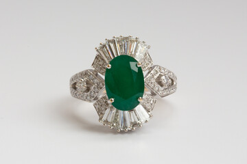A gold ring featuring an oval cut green emerald surrounded by baguette cut diamonds on a clean white background.