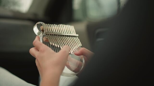 passenger plucking kalimba in car young performer rehearsing for busking, warm sunlight through window, close hand shots, casual jeans, upbeat tinkling, travel practice, focused concentration,