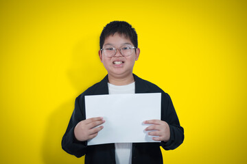 A boy in a business suit holds a white sheet of paper against a yellow gold background.