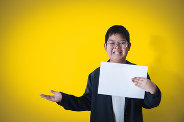 A boy in a business suit holds a white sheet of paper against a yellow gold background.