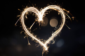Sparkler heart light painting creates glowing romantic shape against dark background with bright sparks and warm illumination for celebration or festive mood