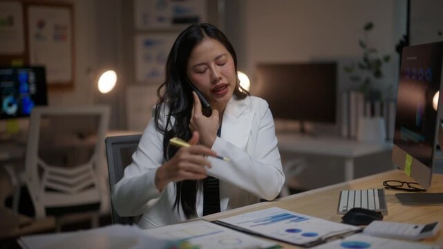 Anxious businesswoman talking on the phone while working late at night in the office. Stressed employee dealing with a difficult customer