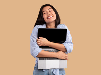 Technology Lover Concept. Happy asian woman hugging laptop with black blank empty screen, holding it tight near chest. Casual lady geek posing isolated over studio background wall, copy space