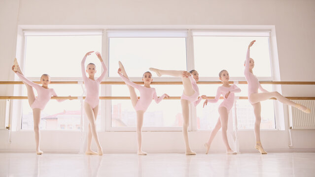 Group of young ballet dancers practicing flexibility exercises at barre. Concept of ballet education ads, group training promotion, children dance school marketing, and enrollment campaign content. - Powered by Adobe