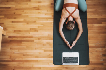 Top view of woman practicing yoga on yoga mat with laptop.