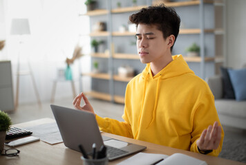 Workplace Stress Management. Calm Korean man meditating with closed eyes in front of laptop pc at home office. Young guy freelancer feeling peaceful and balanced, doing yoga sitting at his desk