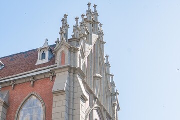 Old Gothic Roman Catholic church, imposing height, numerous pointed arches, spires, stone structure light gray, dark accents, warm glow sunlight from right side, blurred ground, serene atmosphere