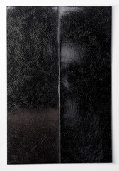 Glossy black photo paper with a deep vertical crease, isolated on a white background. The surface shows strong reflections, texture, and wear, emphasizing damage, folding, and imperfection.