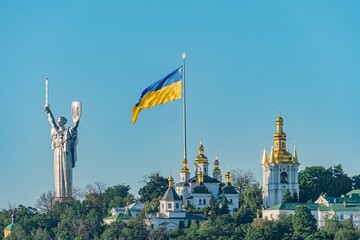 Obraz premium Panoramic view of Kyiv cityscape, clear sky, multiple domed cathedral, modern and traditional architecture, flag blue and yellow, statue